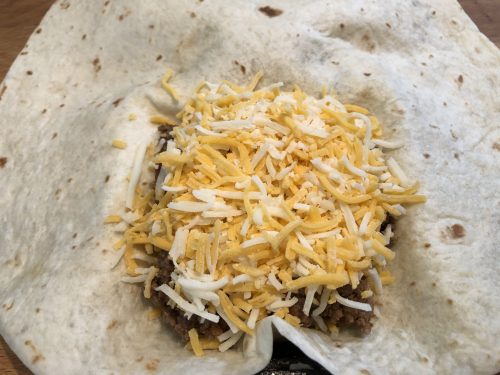 taco meat and shredded cheese on tortilla in pie iron