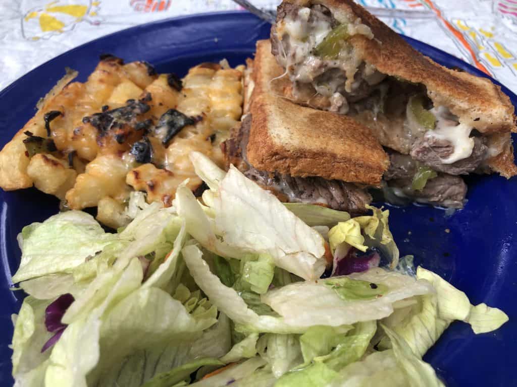 philly cheesesteak with salad and cheesy fries on blue plate