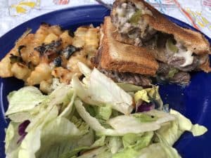 pie iron philly cheesesteak with salad and cheesy fries on blue plate