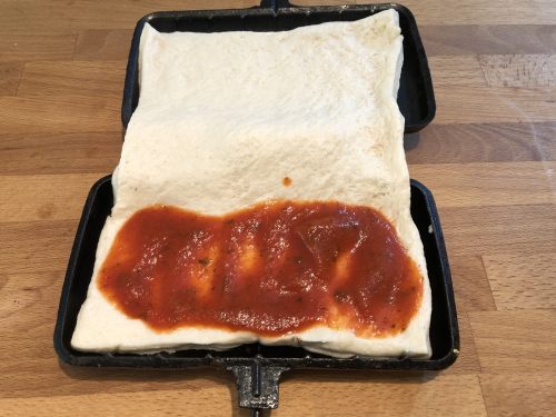 pizza dough with sauce inside of a pie iron
