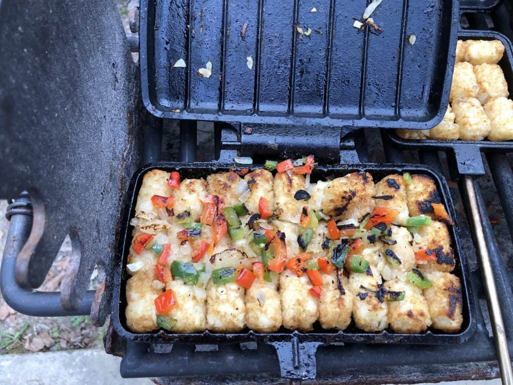 cooked tator tots with peppers and onions in pie iron on grill
