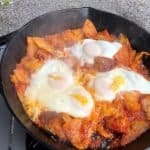 four over easy eggs sitting on top of fried tortillas in red sauce in a cast iron skillet