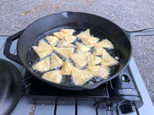 corn tortilla triangles frying in oil in a cast iron skillet on a camp stove