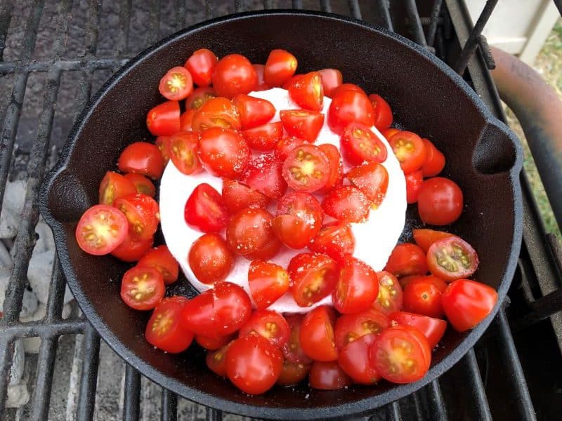 wheel of brie in cast iron skillet with tomatoes on top on grill