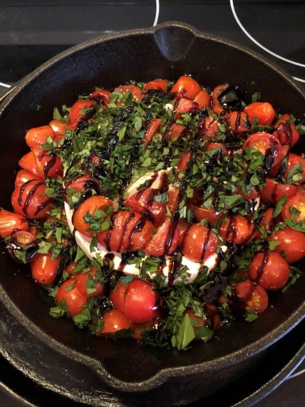 wheel of brie in cast iron skillet with tomatoes, basil, and balsamic glaze on top