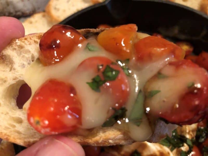 hand holding slice of baguette topped with caprese brie