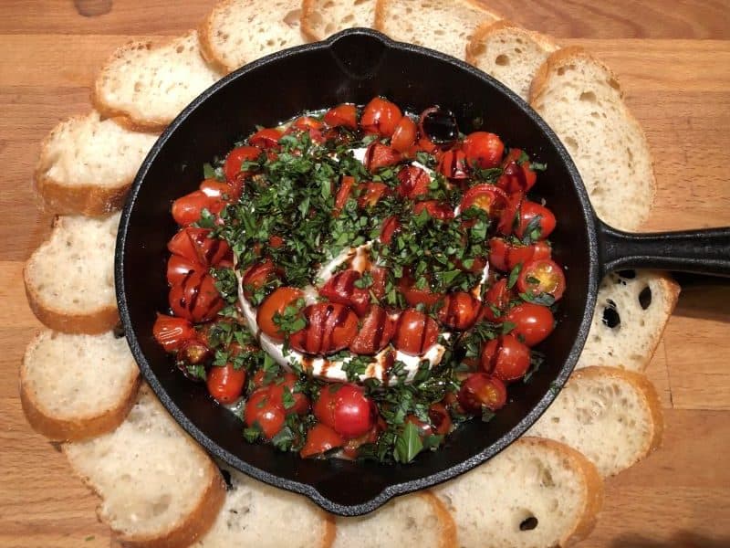 Brie topped with tomatoes, basil, and balsamic in cast iron skillet surrounded by slices of baguette