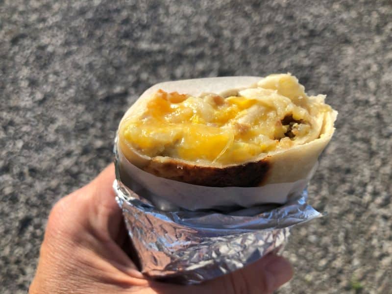 hand holding burrito wrapped in foil outside with sausage potato and green chiles