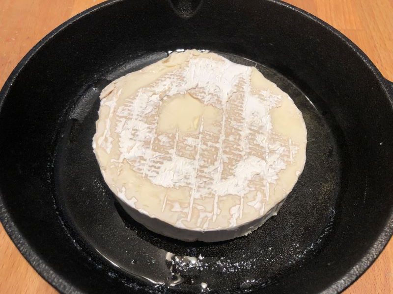 Wheel of brie with top sliced off in cast iron skillet