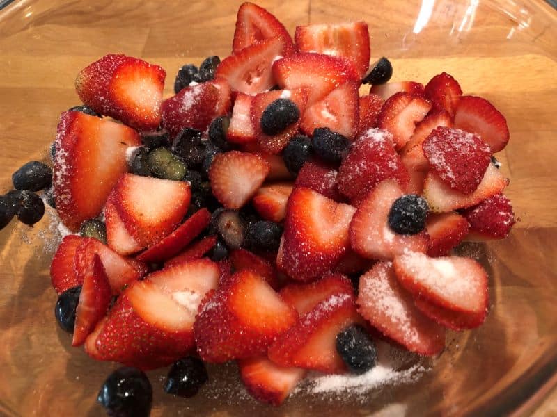 sliced blueberries and strawberries tossed with sugar in glass bowl