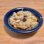 blue bowl with berries, nuts, and couscous on wood background