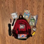 red backpack surrounded by survival items on wood background