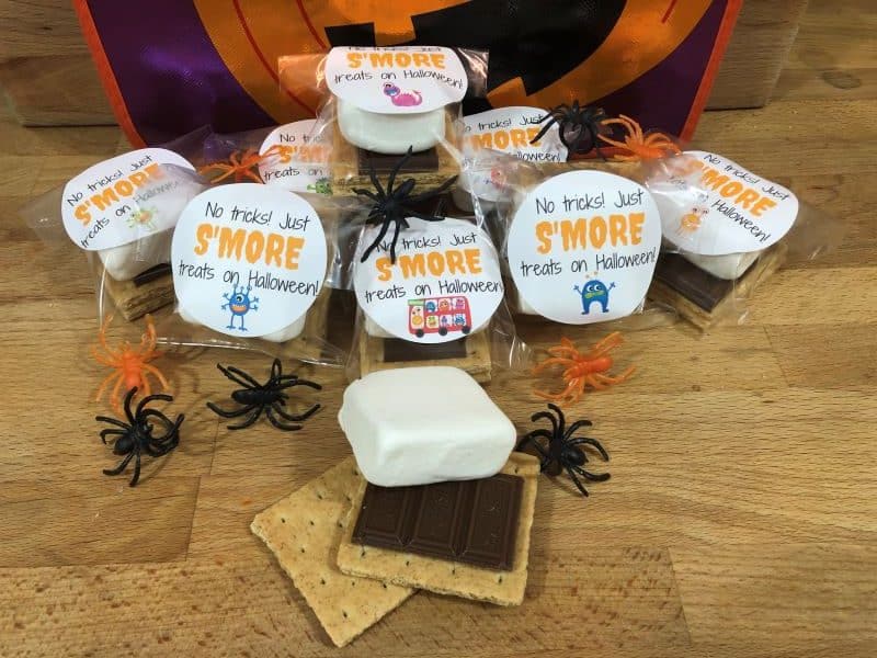 halloween themed s'mores kits with fake spiders and s'mores ingrendients on wood surface