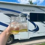 hand holding two drinks in mason jars in front of rv