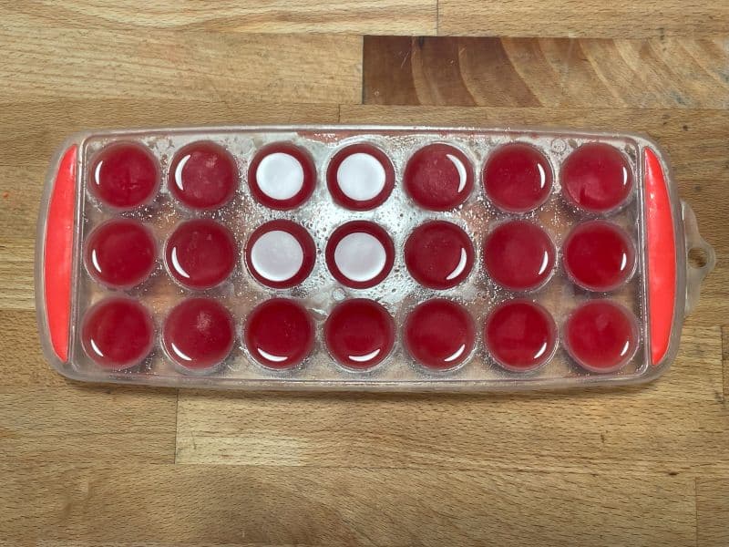 watermelon simple syrup frozen in ice cube tray on wood background